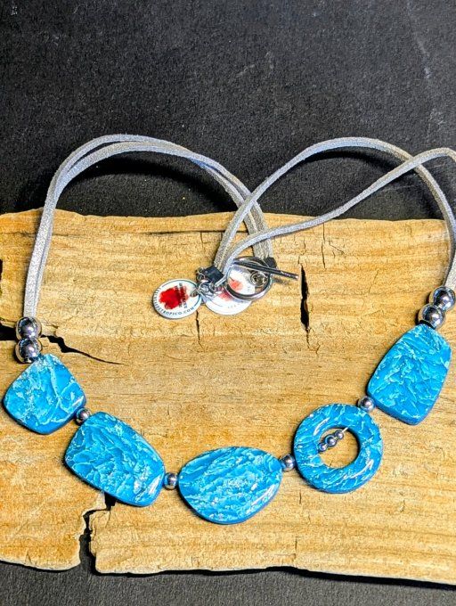 Collier artisanal turquoise et argenté posé sur un support en bois, perles organiques en argile poly
