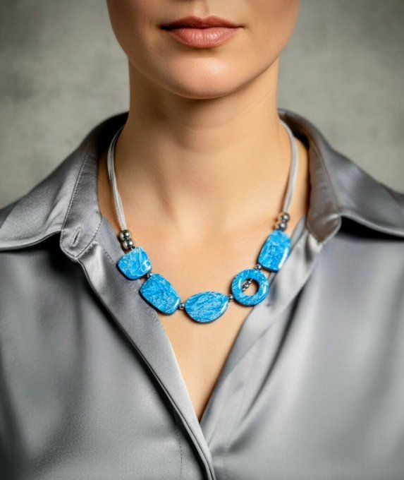 Collier artisanal turquoise et argenté posé sur un support en bois, perles organiques en argile poly